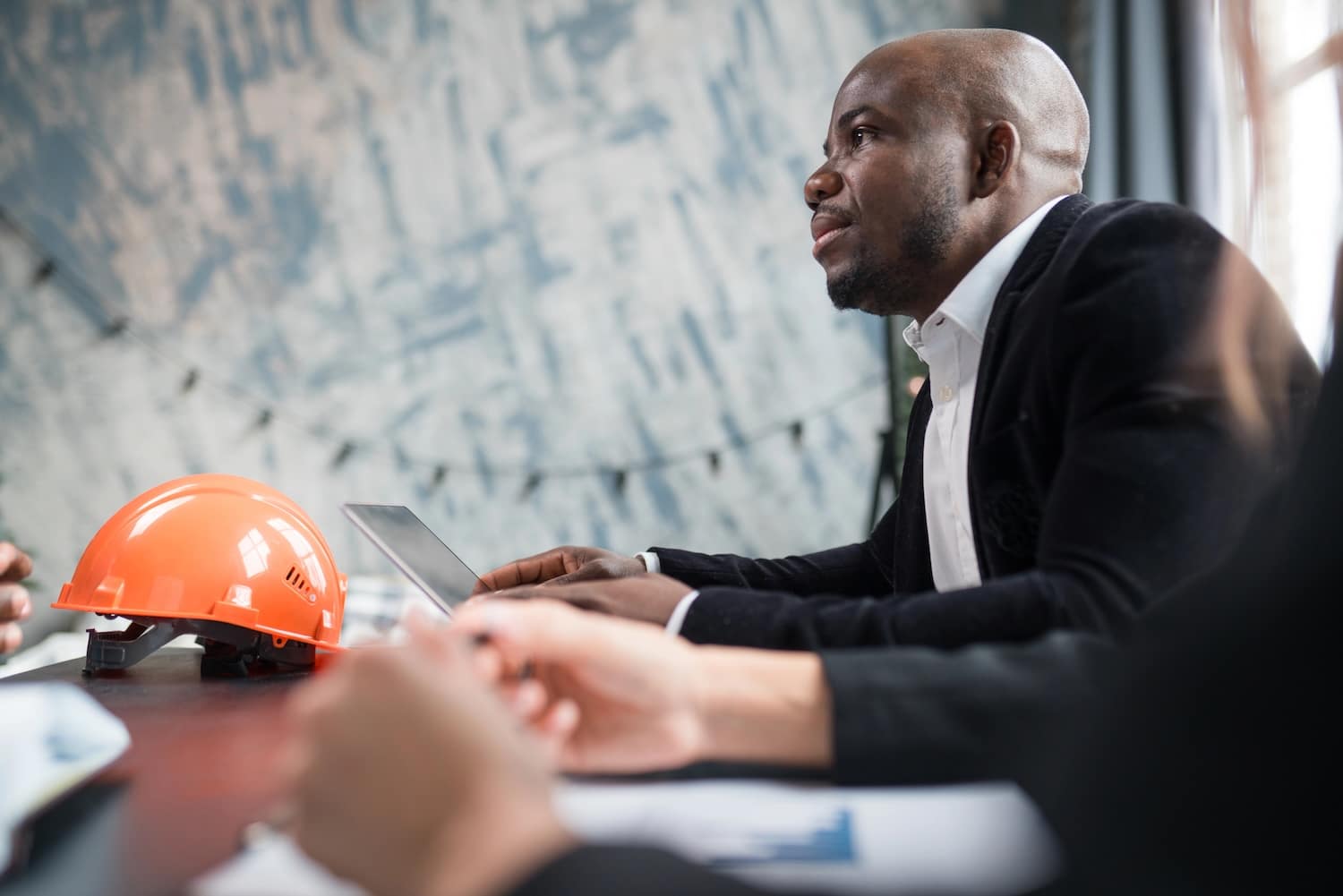 A man african american director of a construction company holds a meeting with colleagues, sits at a table with documents and an orange construction helmet. High quality photo