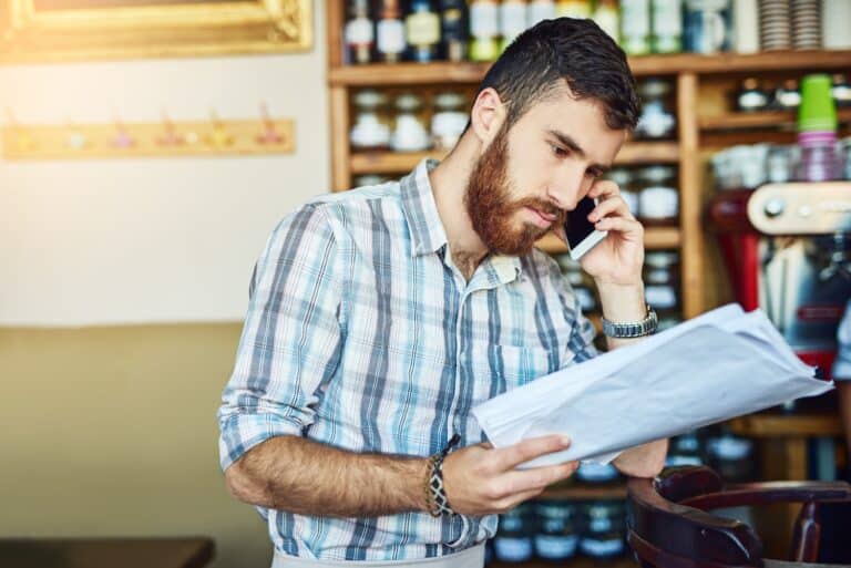 Business owner talking on his cellphone while looking at paperwork