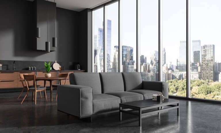 Dark hotel apartment interior with couch and eating table with cabinet shelves, side view. Dining and relax place with panoramic window on New York skyscrapers.